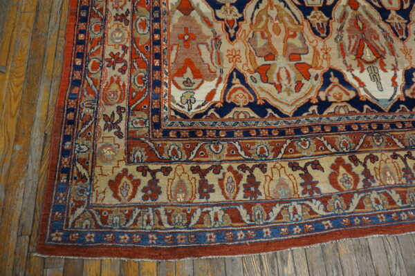 Ornate traditional rug in navy, rust red, and beige lying on distressed wooden floors.