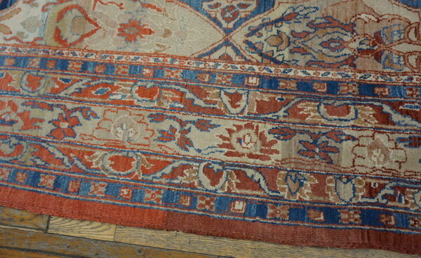 Muted beige, terracotta, and deep blue traditional rug border detailing rests on light hardwood flooring.