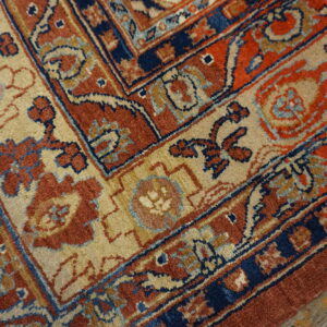 The detailed border of a rust, navy, and tan rug with a floral pattern rests on weathered wood planks.