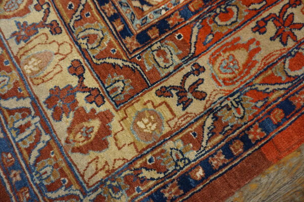 The detailed border of a rust, navy, and tan rug with a floral pattern rests on weathered wood planks.