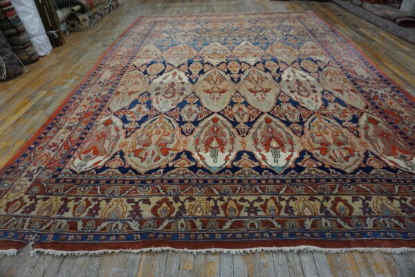 Ornate low-pile rug with red, navy, and cream floral lattice design rests on distressed wood plank flooring.
