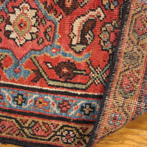 Red, blue, and cream patterned rug folded over, displaying the woven structure on a hardwood floor.
