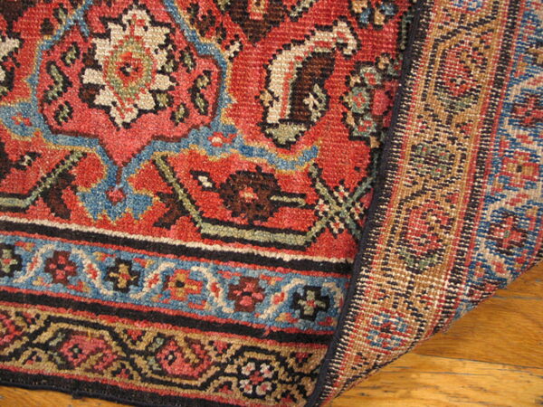 Red, blue, and cream patterned rug folded over, displaying the woven structure on a hardwood floor.