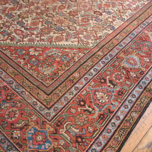 Traditional low-pile rug with red geometric borders and a floral cream center resting on wood flooring.