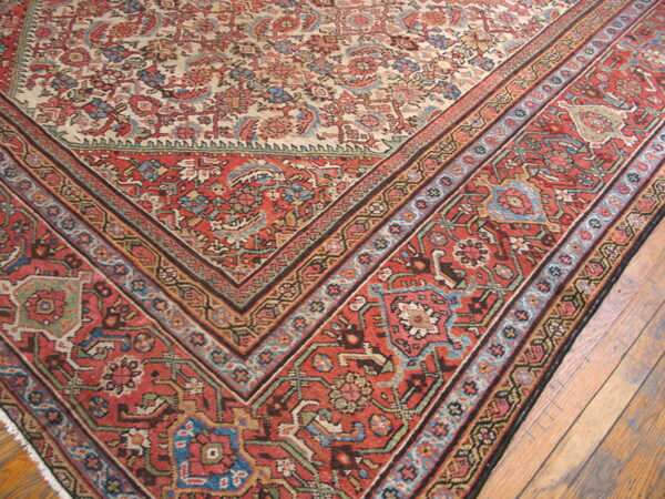 Traditional low-pile rug with red geometric borders and a floral cream center resting on wood flooring.