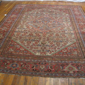 Low-pile patterned rug in muted red, cream, and blue lies on a polished light brown hardwood floor.