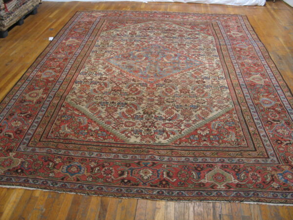 Low-pile patterned rug in muted red, cream, and blue lies on a polished light brown hardwood floor.