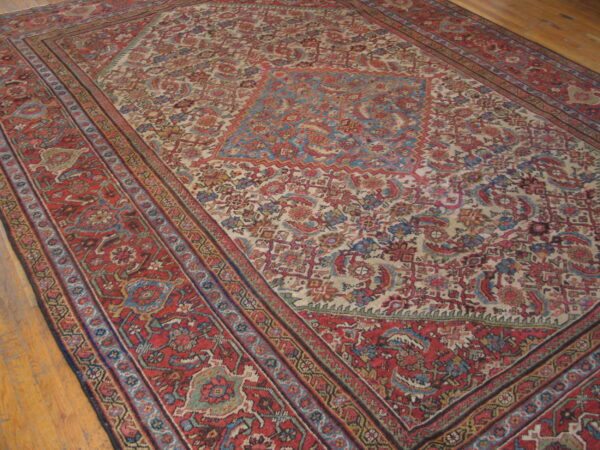 Low-pile traditional red and ivory rug with blue floral patterns resting on light hardwood flooring.