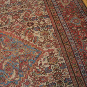 Low-pile rug with a complex floral and geometric pattern in red, blue, and beige on a wood floor.