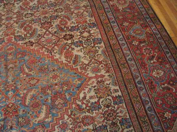 Low-pile rug with a complex floral and geometric pattern in red, blue, and beige on a wood floor.
