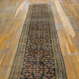 Traditional navy runner rug with stylized gold and red motifs on wide, worn wood planks.