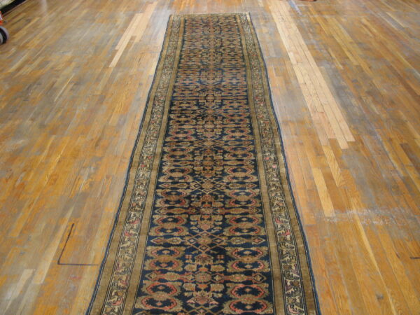 Traditional navy runner rug with stylized gold and red motifs on wide, worn wood planks.