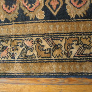 Traditional navy, tan, and coral patterned rug border rests on medium-toned hardwood flooring.