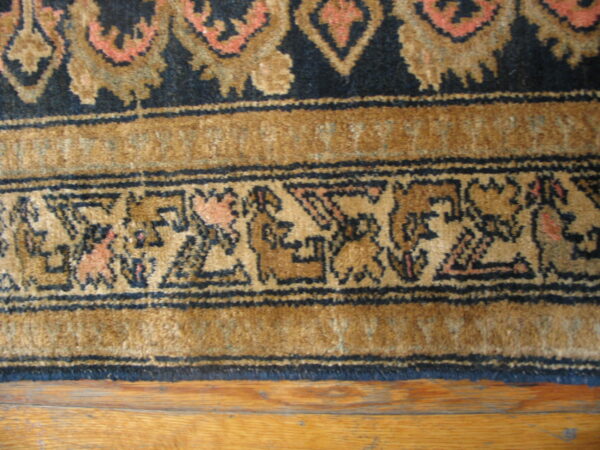 Traditional navy, tan, and coral patterned rug border rests on medium-toned hardwood flooring.