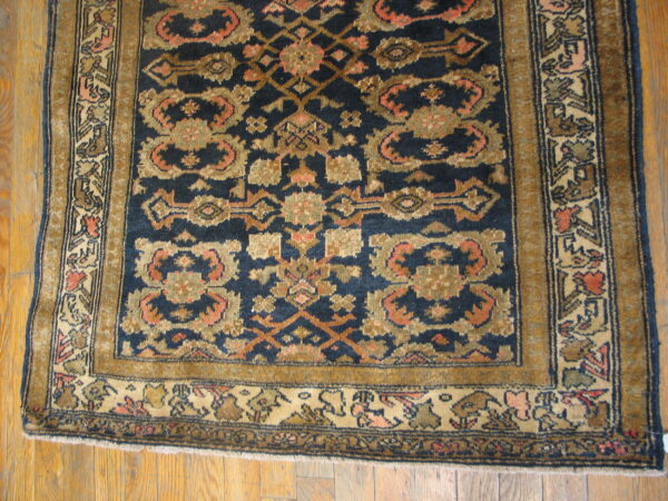 Dark blue rug with stylized gold and terracotta motifs and complex patterned borders on wood floor.