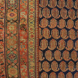 Close-up of a rug with a navy field of repeating red boteh next to a patterned sage and red border.
