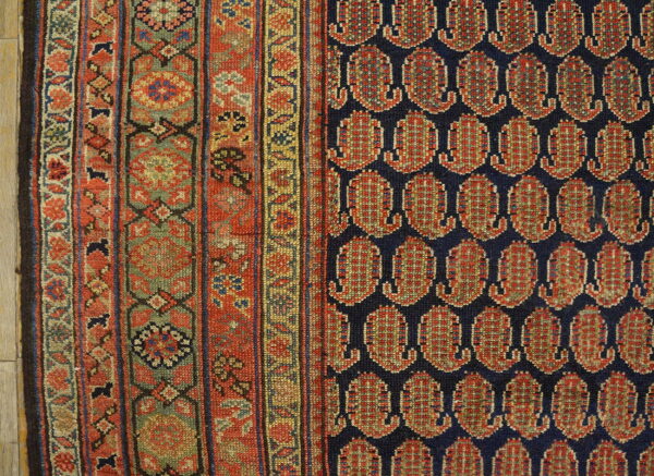 Close-up of a rug with a navy field of repeating red boteh next to a patterned sage and red border.