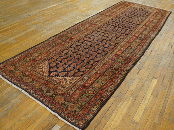 Navy and red patterned runner rug with intricate borders rests on light, wide plank wooden flooring.