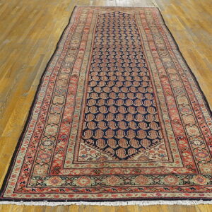 Runner rug with a dark blue central field and red repeating motifs, featuring intricate borders on wood planks.