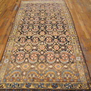 Traditional brown rug with repeating orange and gold motifs displayed on textured wooden flooring.