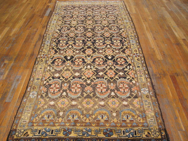 Traditional brown rug with repeating orange and gold motifs displayed on textured wooden flooring.