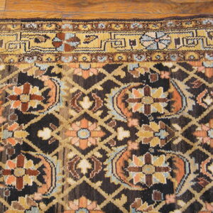 Dark rug detail shows a brown trellis, gold and orange florals, and a wide border against wood flooring.