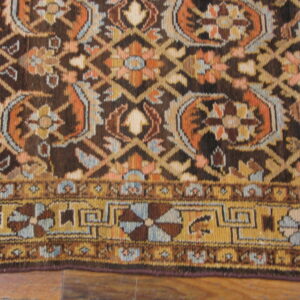 Ornate, dark brown rug featuring detailed floral designs in rust, gold, and light blue on a wood floor.