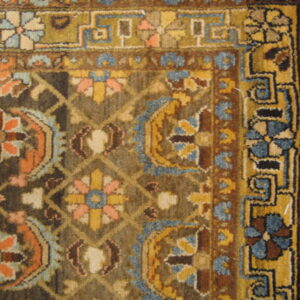 Traditional rug detail showing dark brown, gold, blue, and peach floral motifs within complex geometric borders.