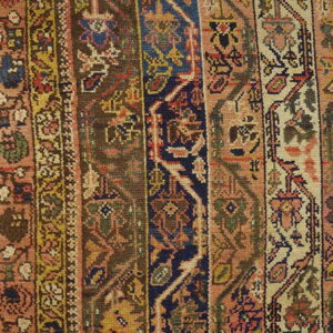 A close-up of a low-pile rug showing vertical geometric borders in navy, terracotta, brown, and cream tones.