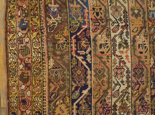 A close-up of a low-pile rug showing vertical geometric borders in navy, terracotta, brown, and cream tones.