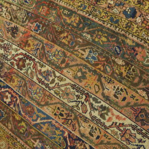 Striped rug pattern in pink, rust, navy, green, and cream lies diagonally on light hardwood flooring.