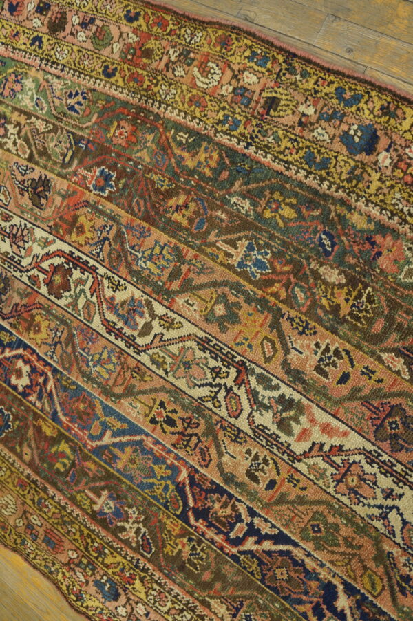 Striped rug pattern in pink, rust, navy, green, and cream lies diagonally on light hardwood flooring.