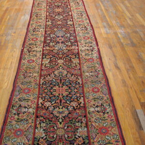 Long runner rug with navy, red, and gold traditional floral pattern displayed on strip hardwood flooring.