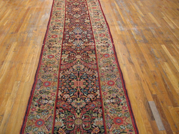 Long runner rug with navy, red, and gold traditional floral pattern displayed on strip hardwood flooring.