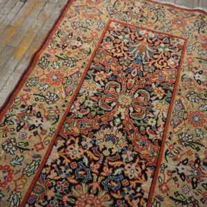 Beige and navy low-pile rug with red and blue intricate floral patterns on worn wood plank flooring.