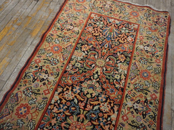 Beige and navy low-pile rug with red and blue intricate floral patterns on worn wood plank flooring.