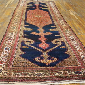 Traditional runner rug with a central orange and navy medallion on light, worn wooden floorboards.