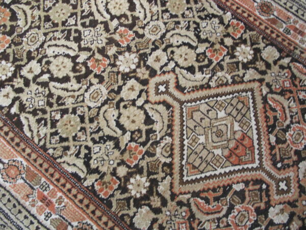 Close-up of a multi-colored rug with dark brown, beige, and orange floral and geometric patterns.