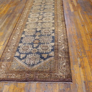 A long runner rug featuring a deep blue geometric pattern and tan borders, placed on distressed wooden floors.