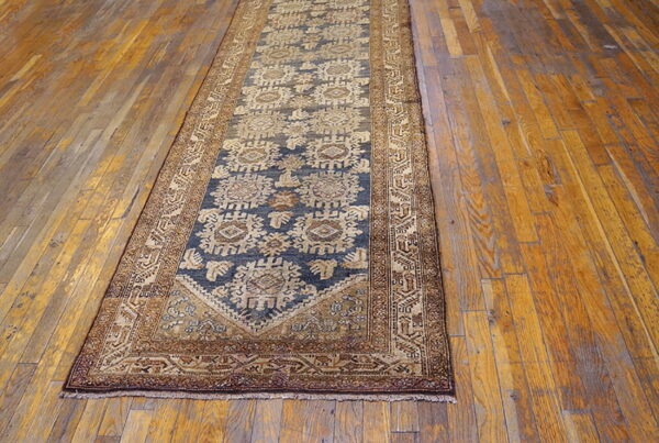 A long runner rug featuring a deep blue geometric pattern and tan borders, placed on distressed wooden floors.