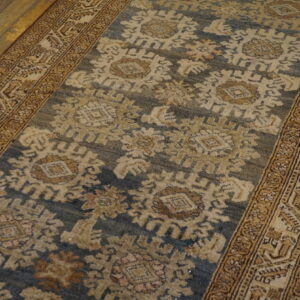 Close-up of a blue and beige patterned low-pile runner rug with ornate golden borders on rustic wood flooring.
