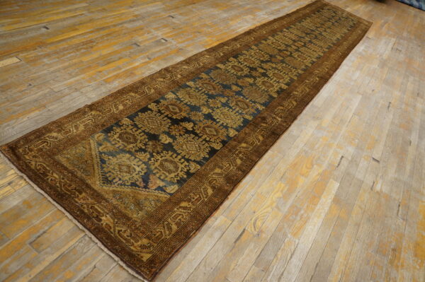Low-pile blue and gold runner rug with geometric designs displayed on distressed wide plank flooring.