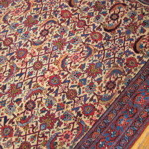 Low-pile area rug with a dense red, blue, and cream traditional design over aged wood floorboards.
