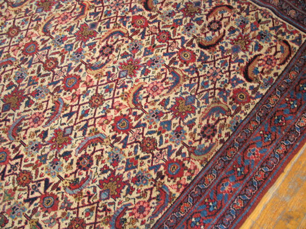 Low-pile area rug with a dense red, blue, and cream traditional design over aged wood floorboards.