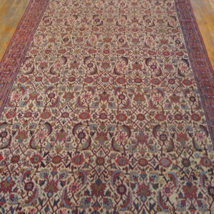 Low-pile rug with a dense cream and red floral geometric pattern covers light wood plank flooring.