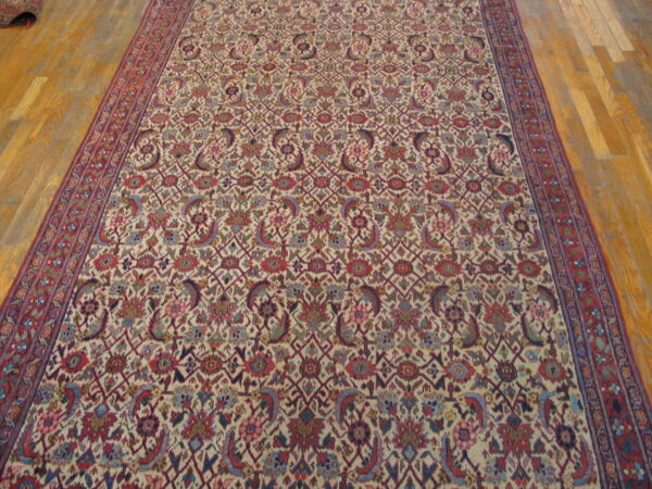 Low-pile rug with a dense cream and red floral geometric pattern covers light wood plank flooring.