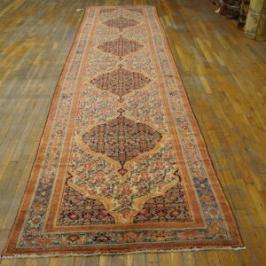 Very long runner rug in rust, navy, and cream patterns on a distressed light brown wood floor.