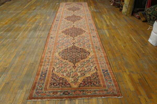 Very long runner rug in rust, navy, and cream patterns on a distressed light brown wood floor.