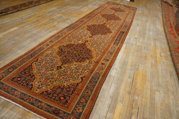 Traditional runner rug in cream, red, and blue with three dark medallions on distressed wood floorboards.