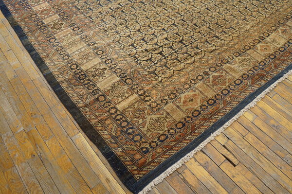Tan and dark blue patterned rug with complex rustic borders resting on aged wooden floorboards.